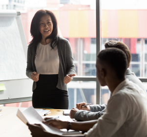 Supportive Leadership (1) Team leader presenting work in an office presenting work to two other colleagues who are watching attentively.